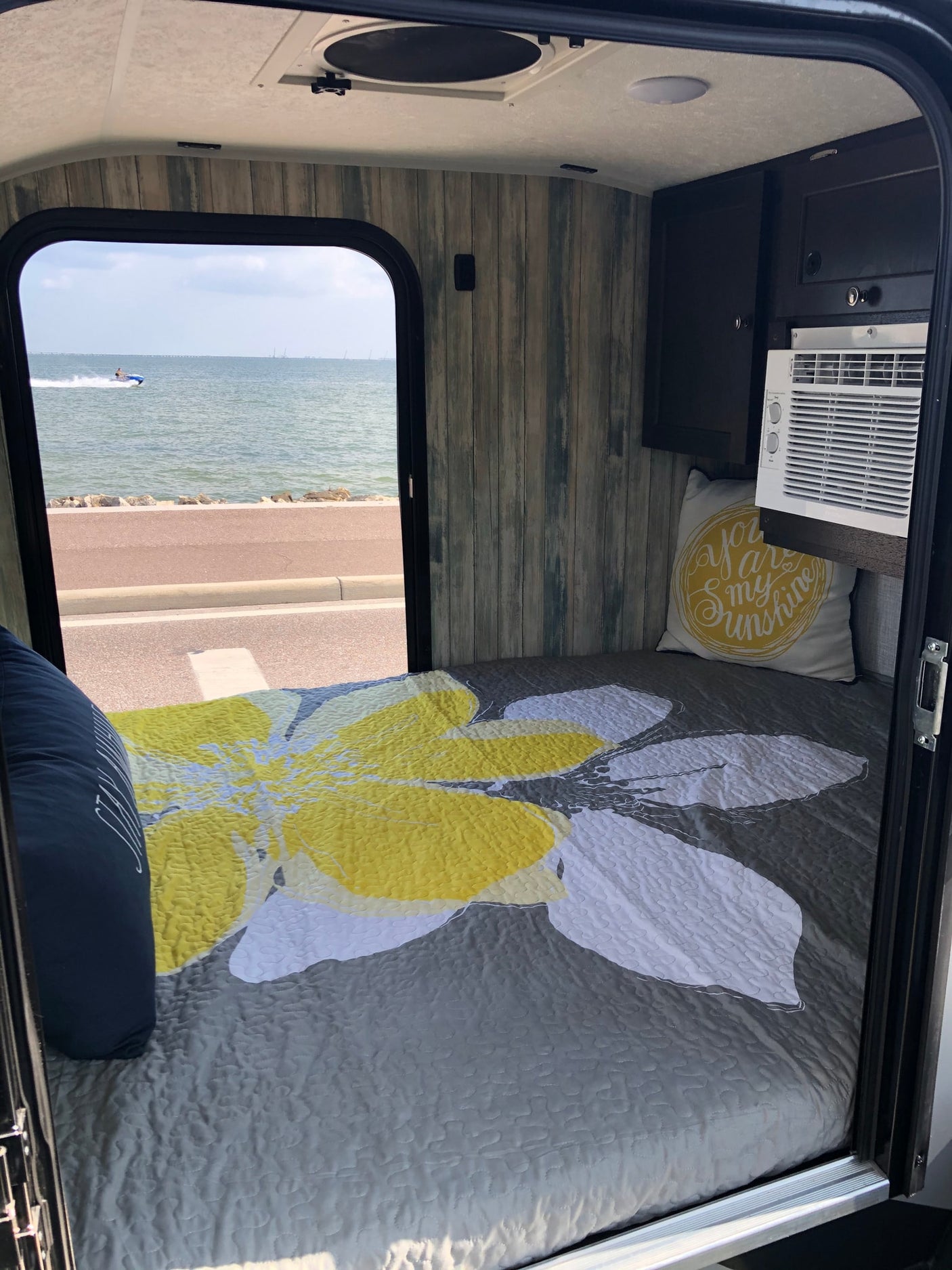 Cozy RV rental interior with a comfortable bed, AC unit, and a scenic waterfront view with a jet ski.