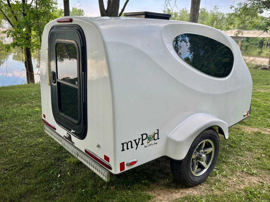 Compact white myPod travel trailer, great for an RV rental, parked by a river with trees. Perfect for camping trips.