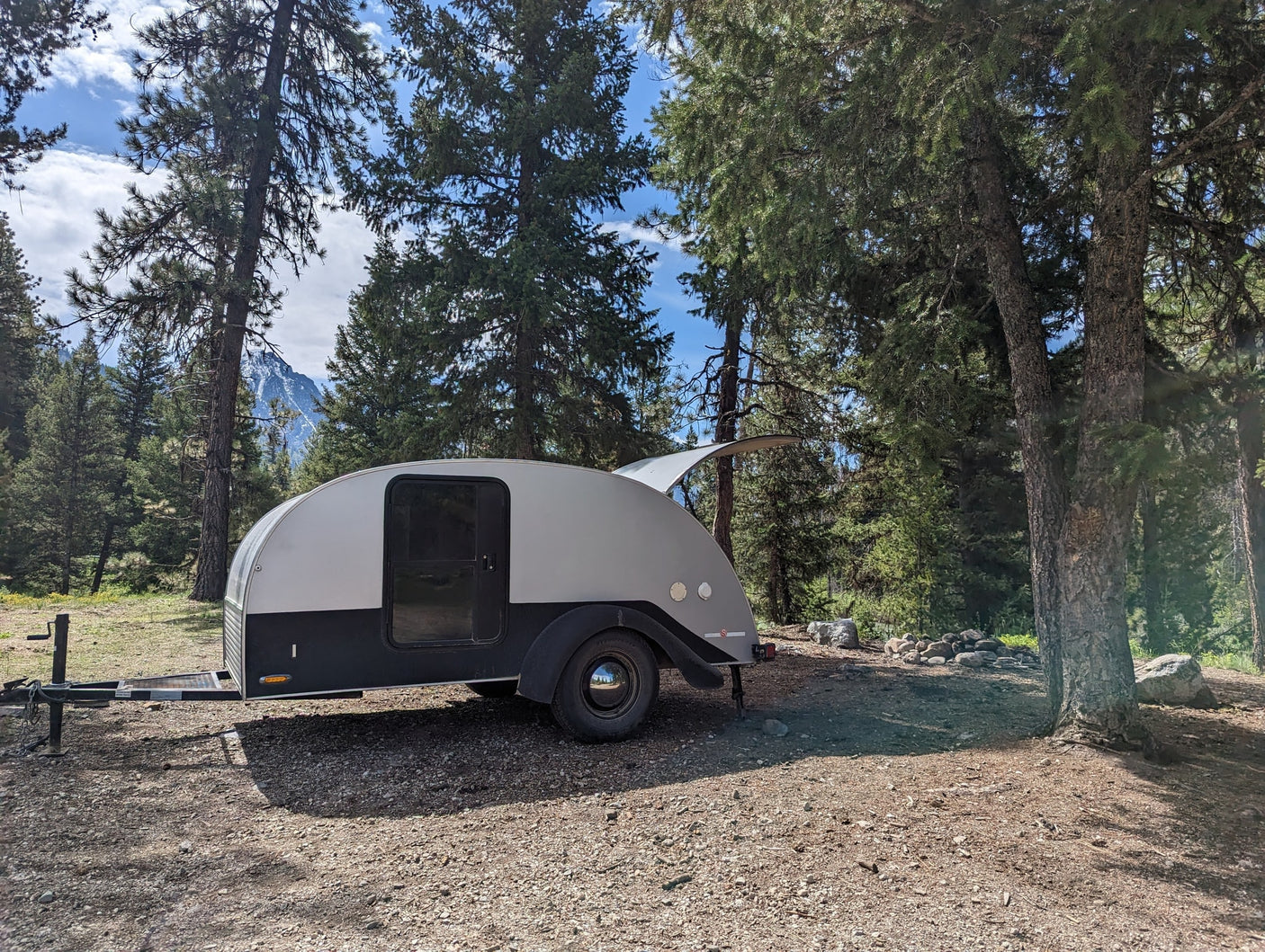 Experience camping! A stylish grey teardrop RV rental parked on a forest campsite with mountain views.