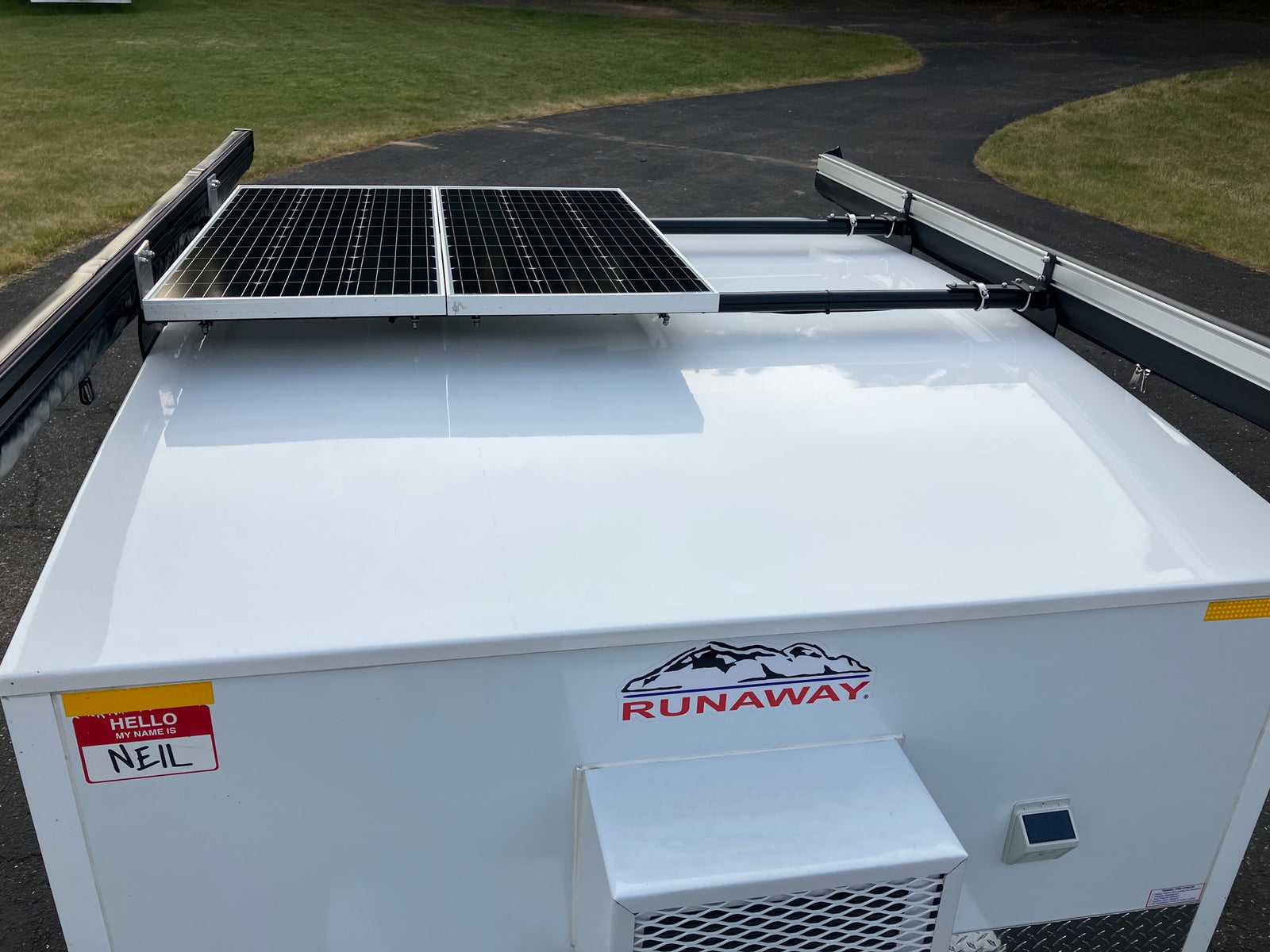 White Runaway RV rental with solar panels & awning on roof. Features a 'Hello, my name is Neil' sticker.
