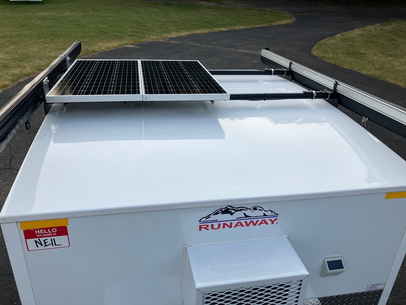 White Runaway RV rental with solar panels & awning on roof. Features a 'Hello, my name is Neil' sticker.