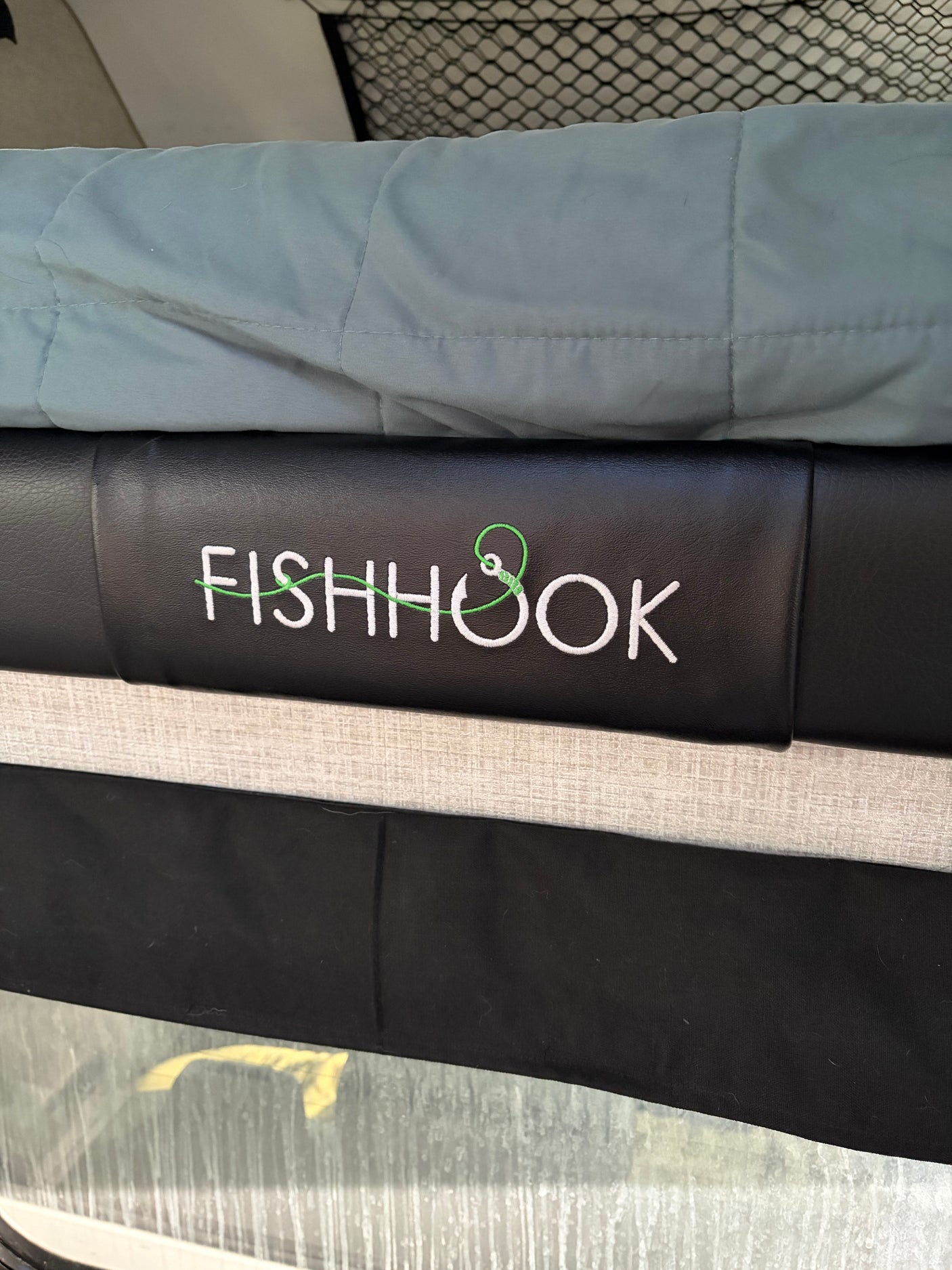 RV rental interior: black upholstery with "FISHHOOK" embroidered, featuring a green line and hook. Blue blanket & window hint at outdoor travel.
