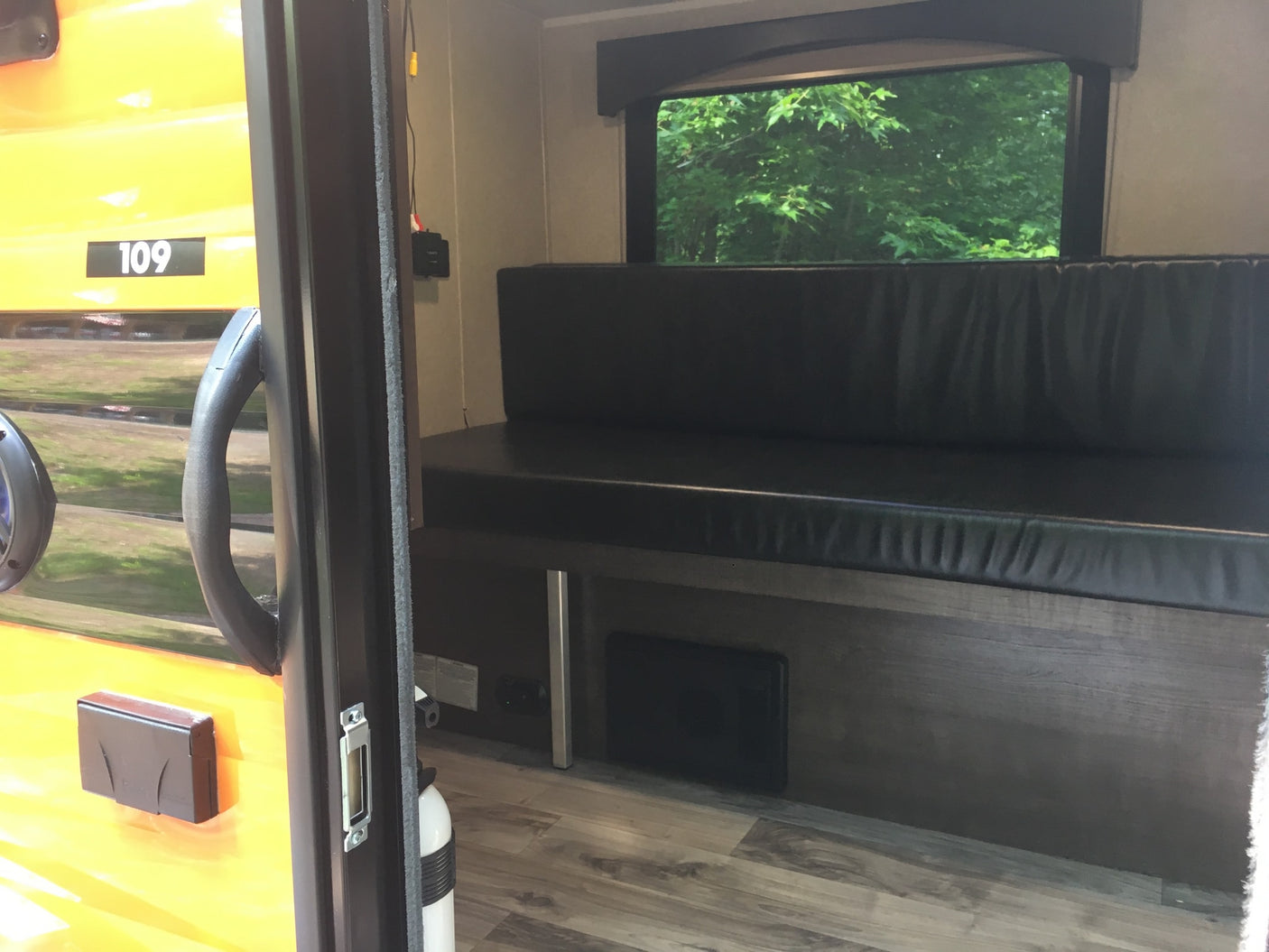 Step inside this RV rental: view of a comfy bench, window with trees, and the bright yellow "109" exterior.