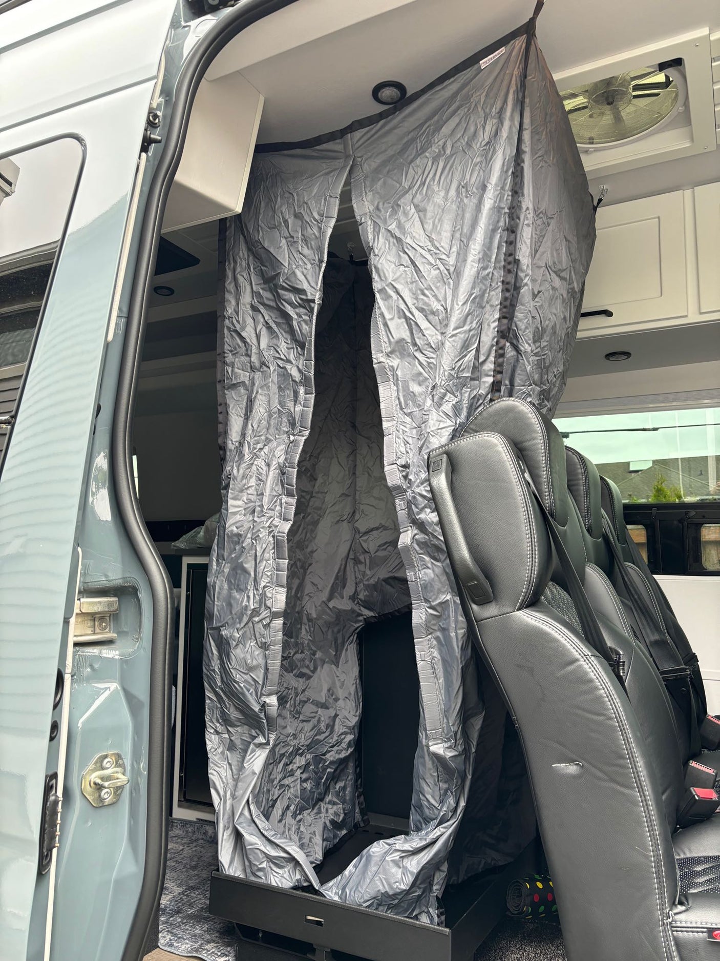 RV rental interior: Gray fabric privacy enclosure, black passenger seats, and open side door visible in this camper van.