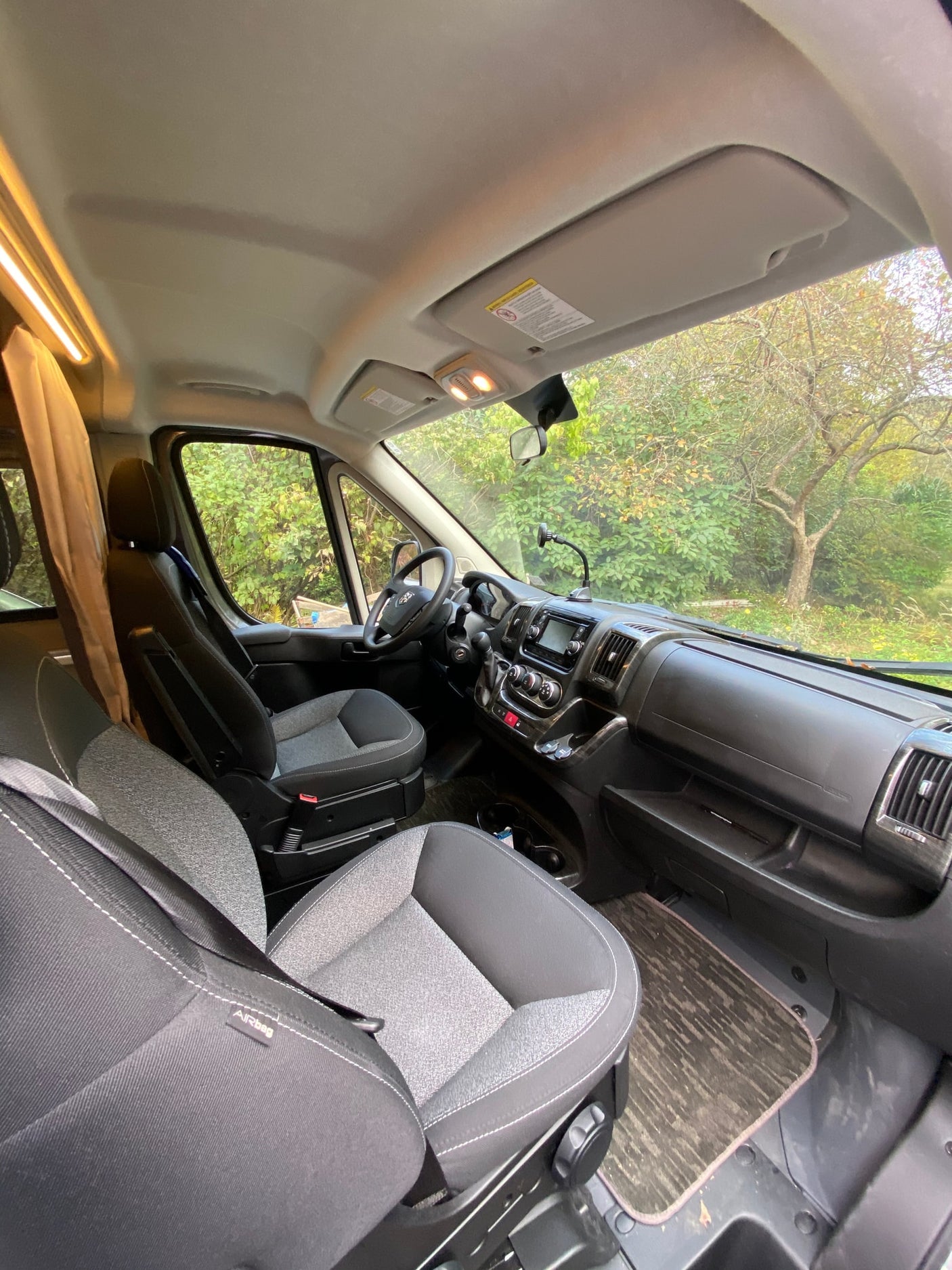 and an illuminated camper setup under the trees.|Experience autumn beauty in an RV rental! This camper van is set up at a vibrant fall campsite with a picnic table.|Inside an RV rental: spacious front cab with seats