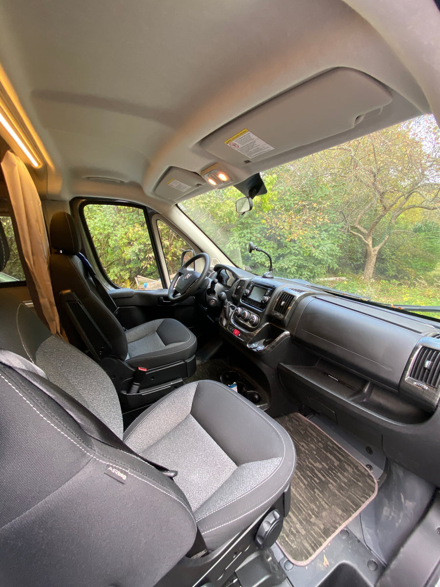 and an illuminated camper setup under the trees.|Experience autumn beauty in an RV rental! This camper van is set up at a vibrant fall campsite with a picnic table.|Inside an RV rental: spacious front cab with seats