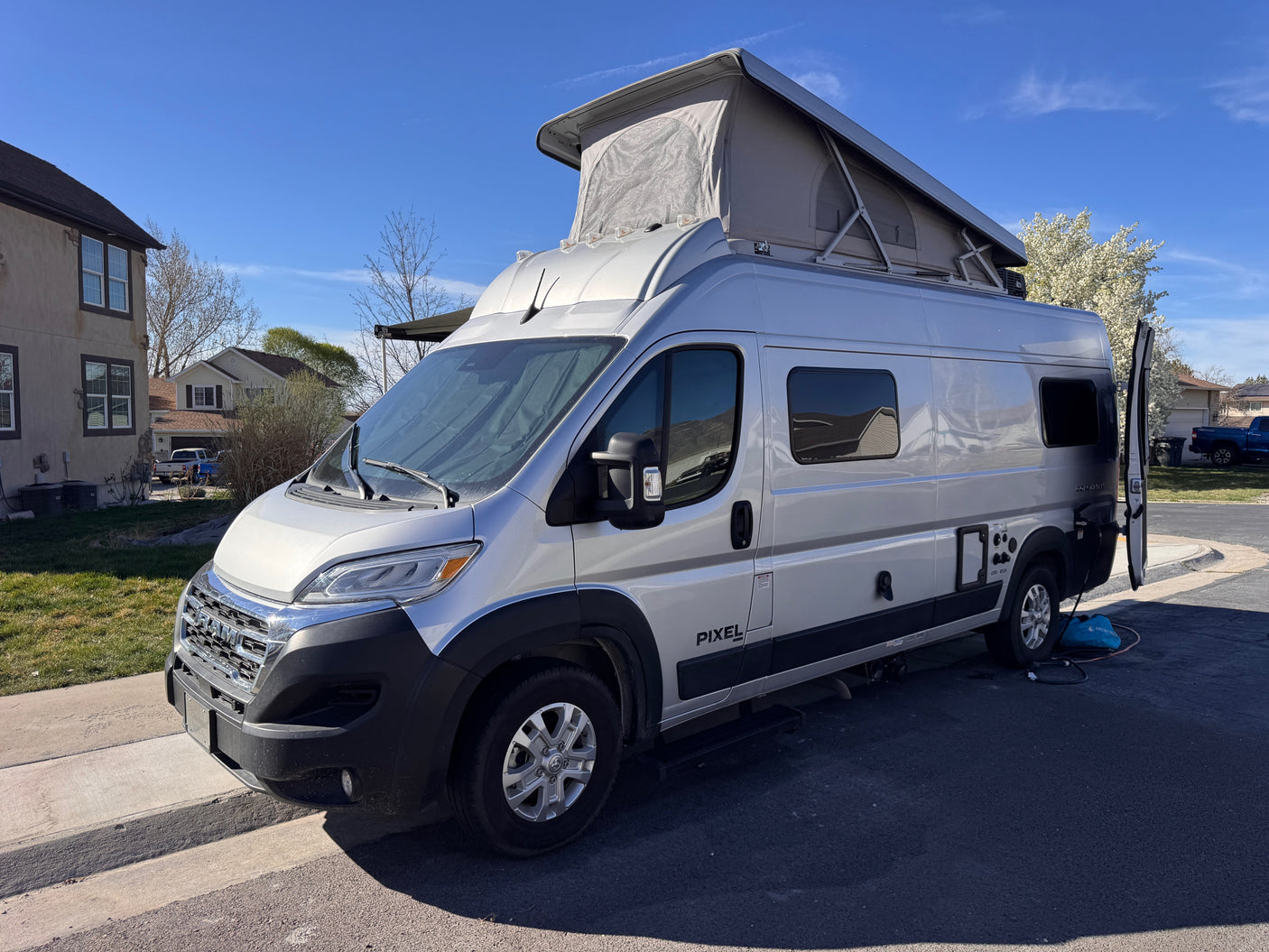 This silver pop-top camper van, branded "Pixel" and ideal for an rv rental, is parked outdoors on a sunny day.