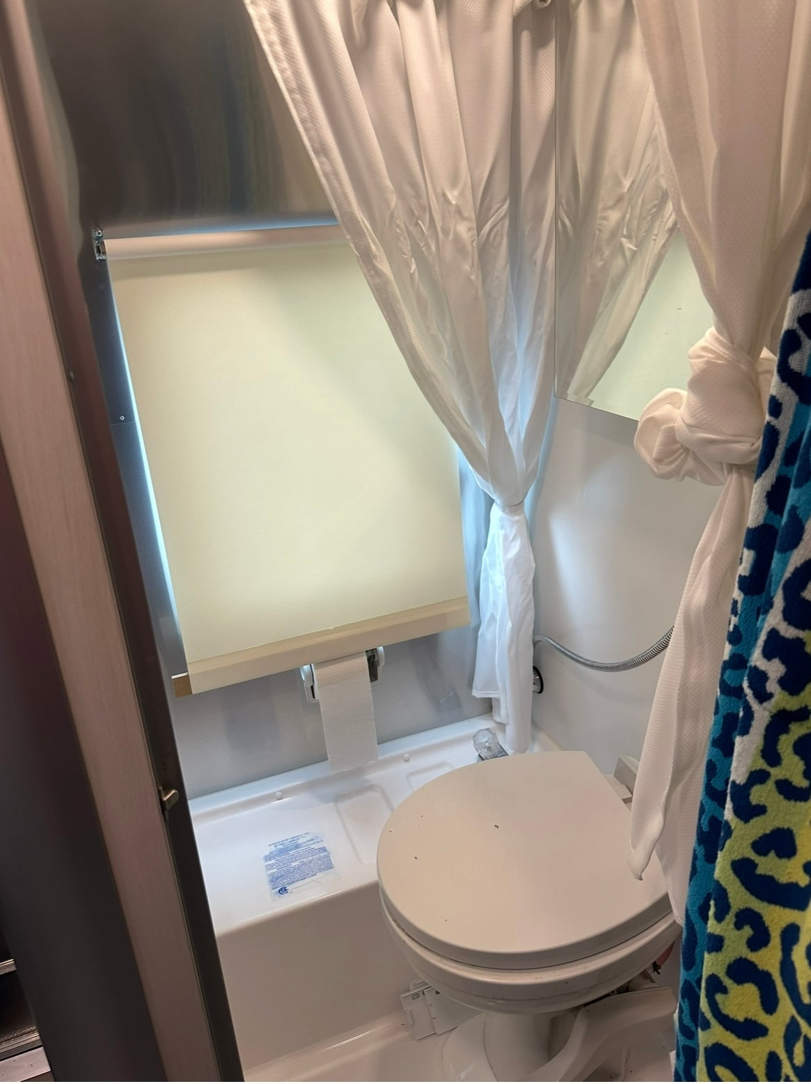 This RV rental's compact bathroom features a toilet, integrated shower, and mirror, optimized for small spaces.