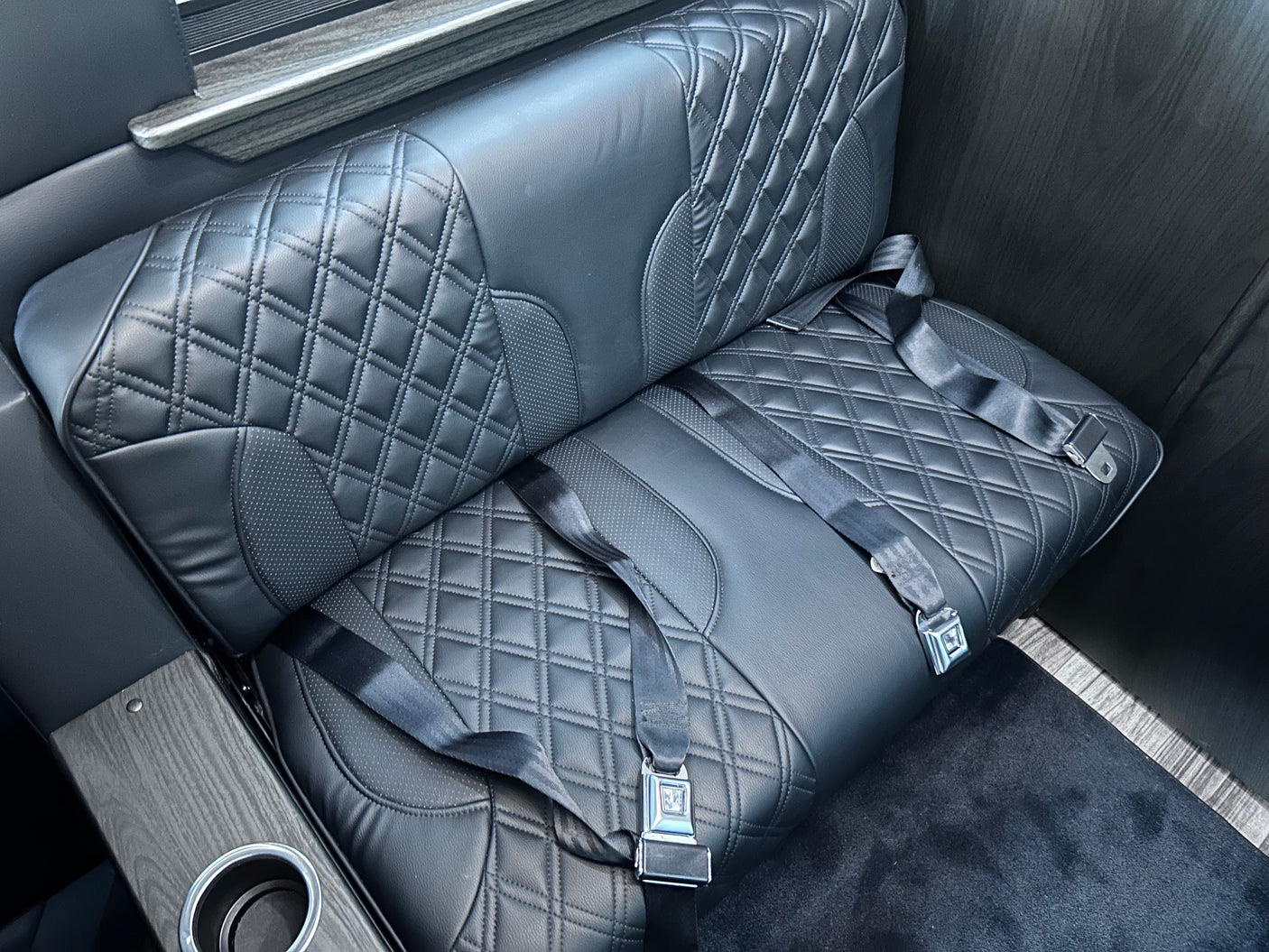Luxurious black quilted leather seating with safety belts and wood-grain console, ideal for your RV rental comfort.