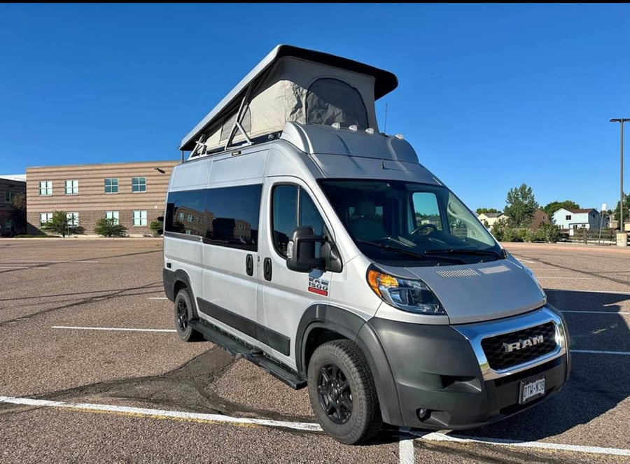 surrounded by trees.|This silver Ram ProMaster camper van