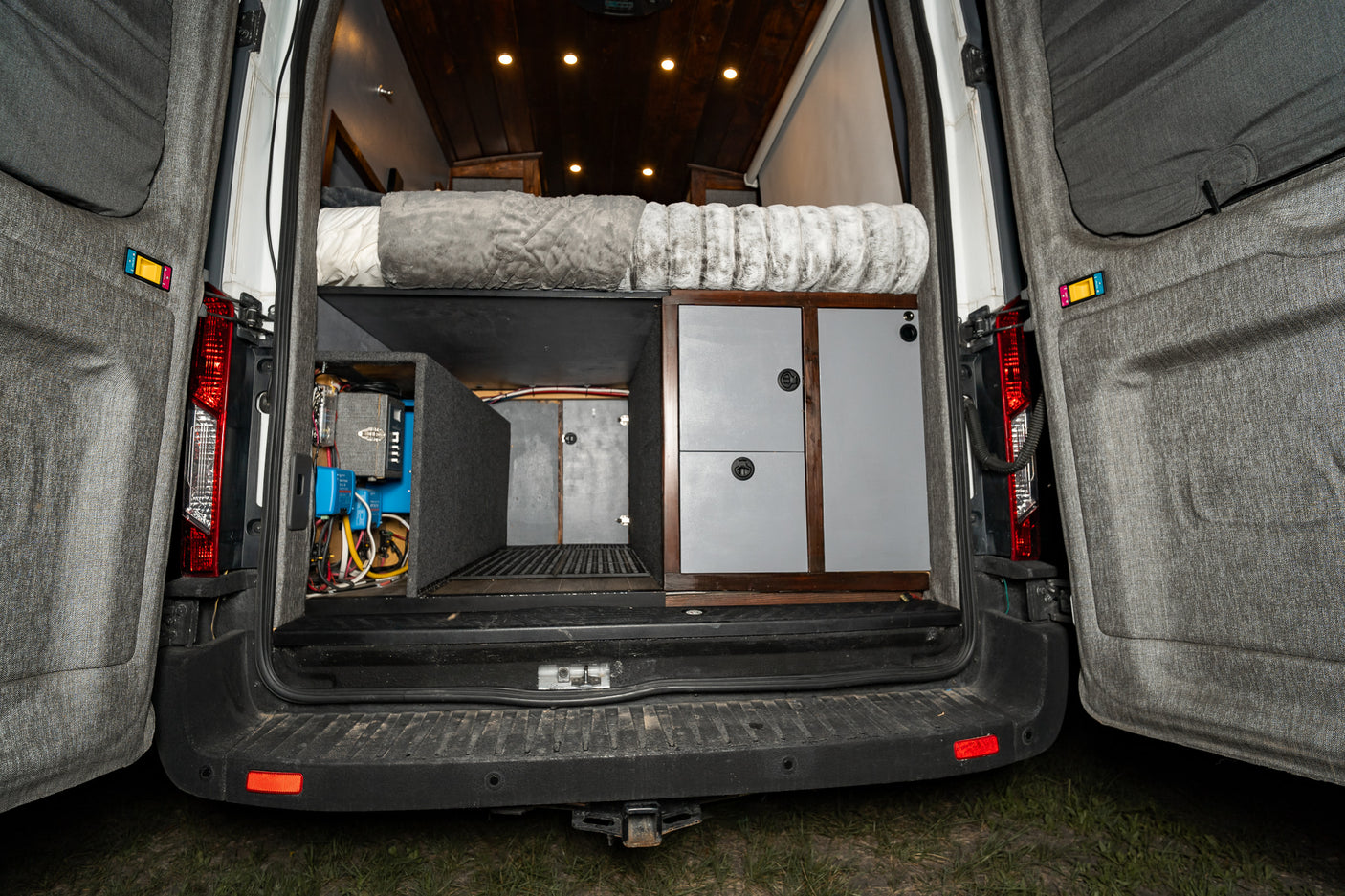 Inside an RV rental camper van: rear view showing a bed, built-in storage, and the electrical system on the left.
