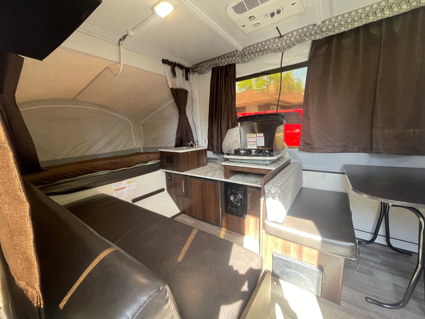 Inside this pop-up camper rv rental: a compact kitchen with stove, sink, adjacent dining area, and a comfortable bed. — photo 5