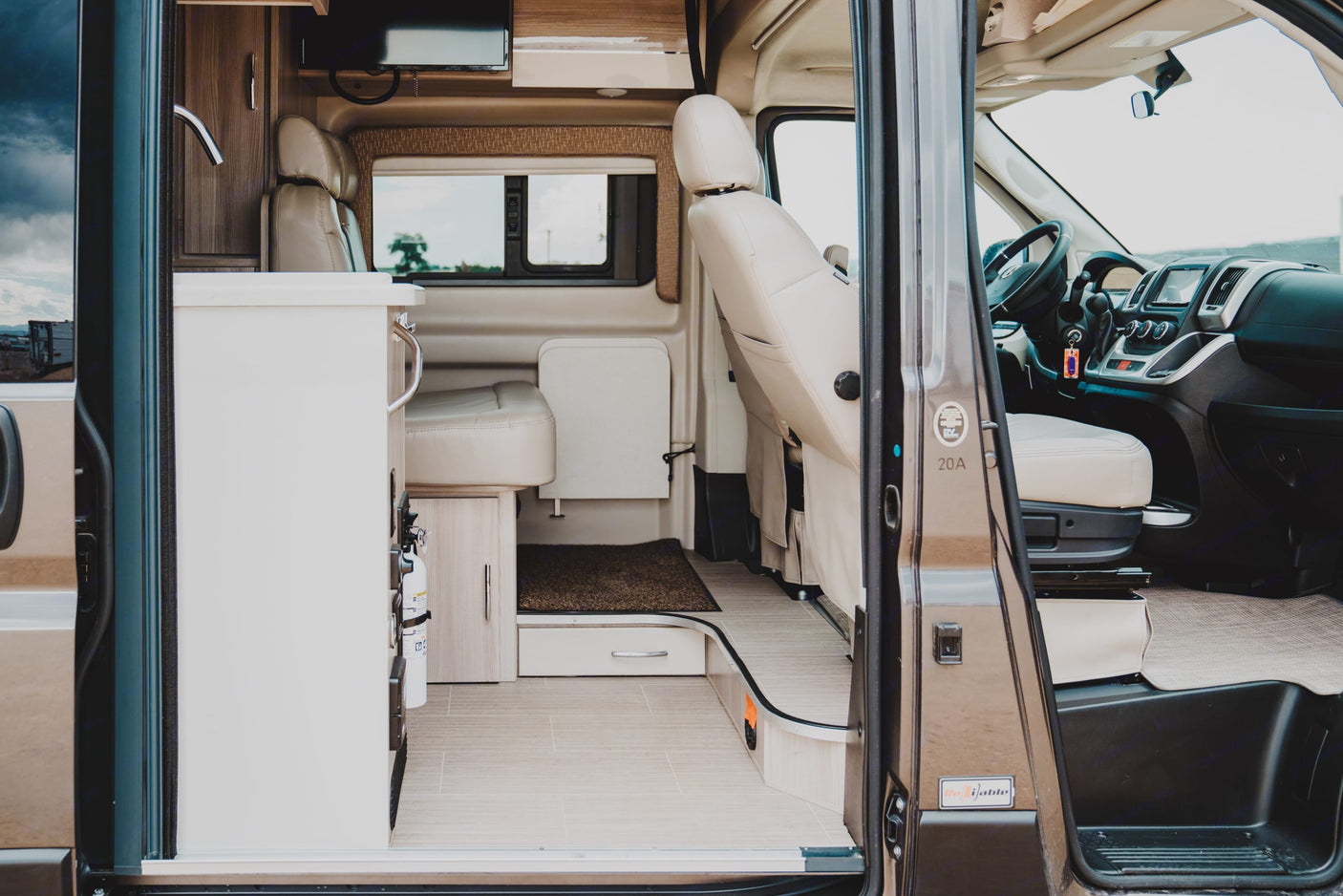 Spacious rv rental interior seen from the open side door, highlighting the living area, kitchenette, and driver's cabin.