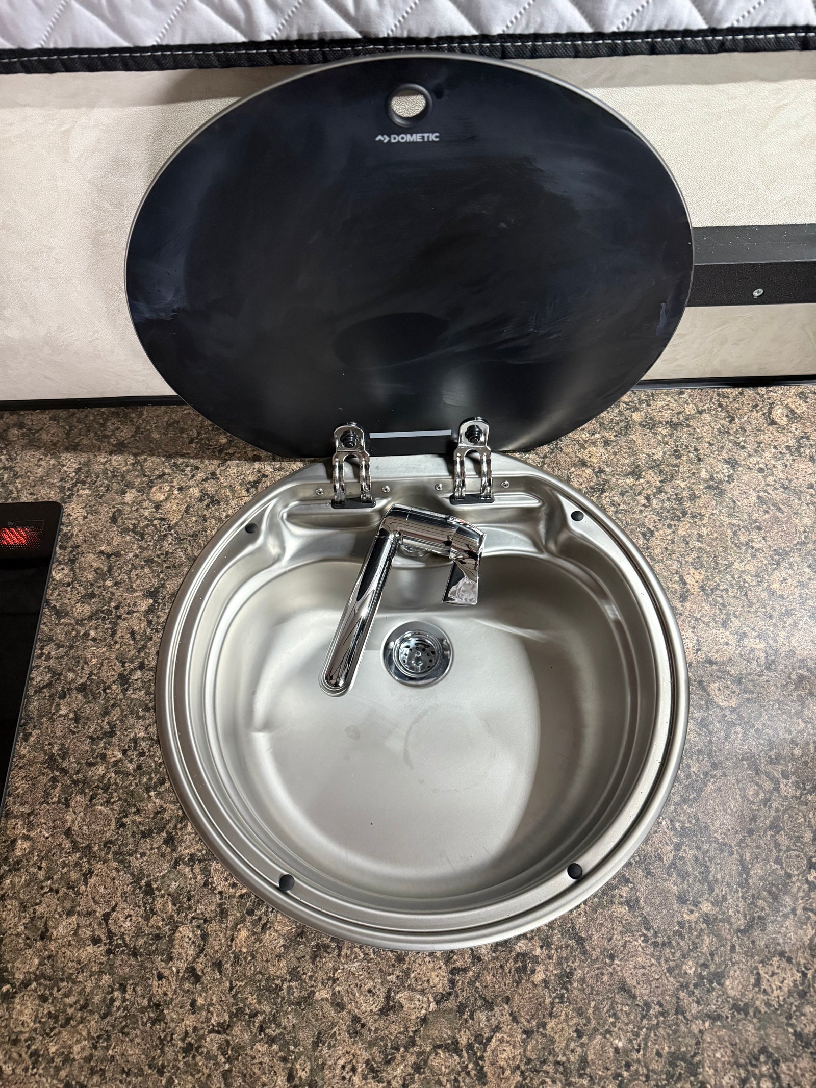 Compact Dometic stainless steel sink and faucet with open lid on a patterned countertop, perfect for your rv rental adventure.