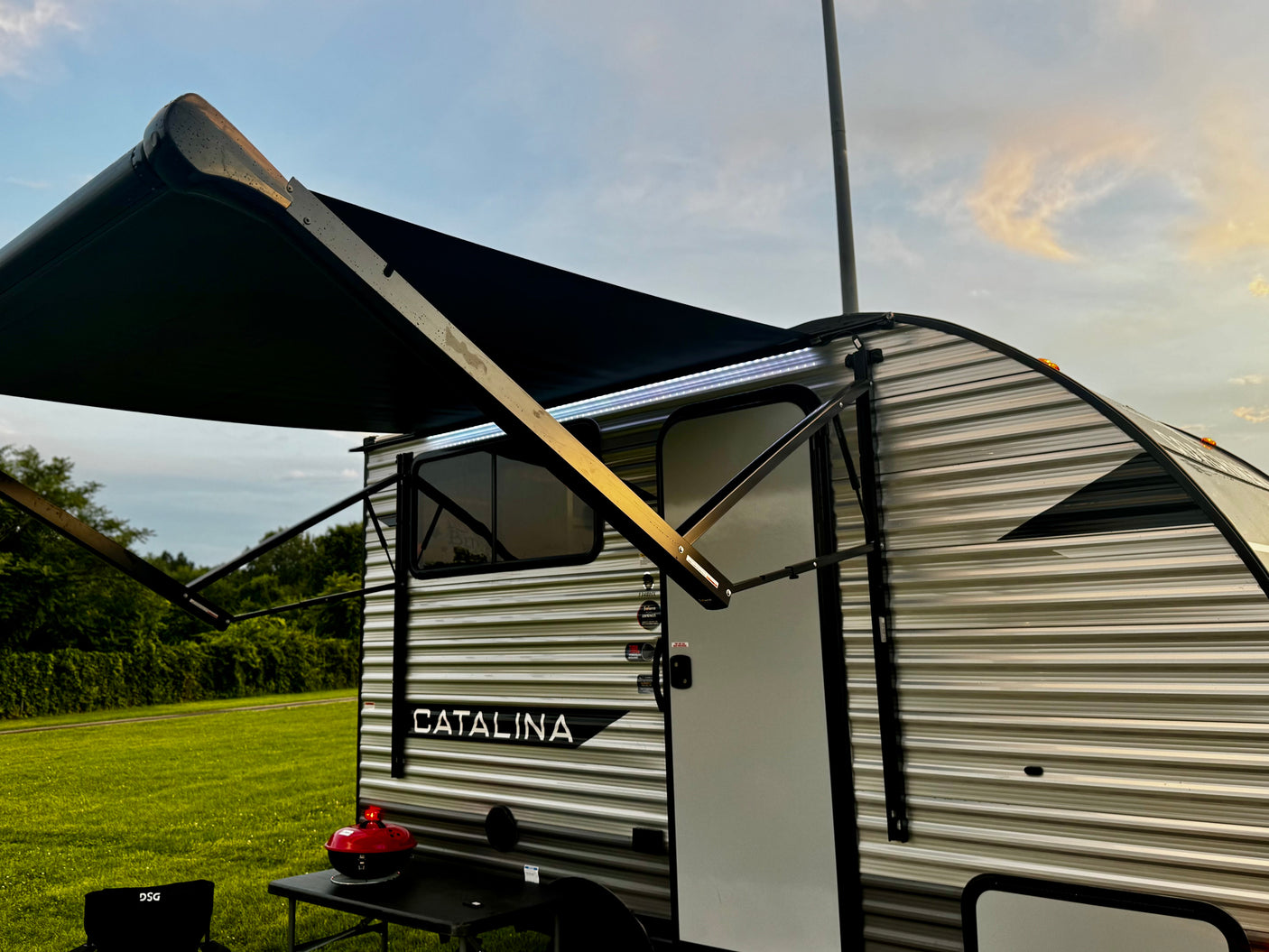 RV rental: Catalina travel trailer with illuminated awning, grill, and chair at a grassy campsite.
