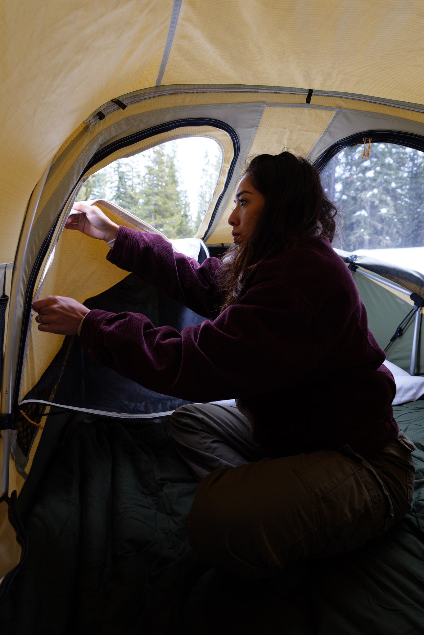 Inside a cozy tent, a person adjusts the window, enjoying the snowy camp view. Enhance your outdoor adventure with an RV rental!