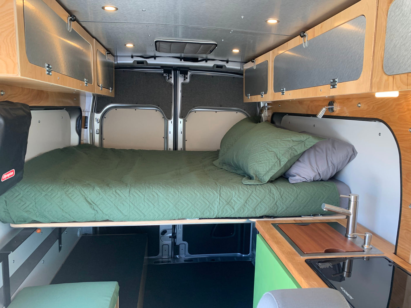 Cozy RV rental interior with a comfortable bed, compact kitchen, and overhead cabinets for storage.