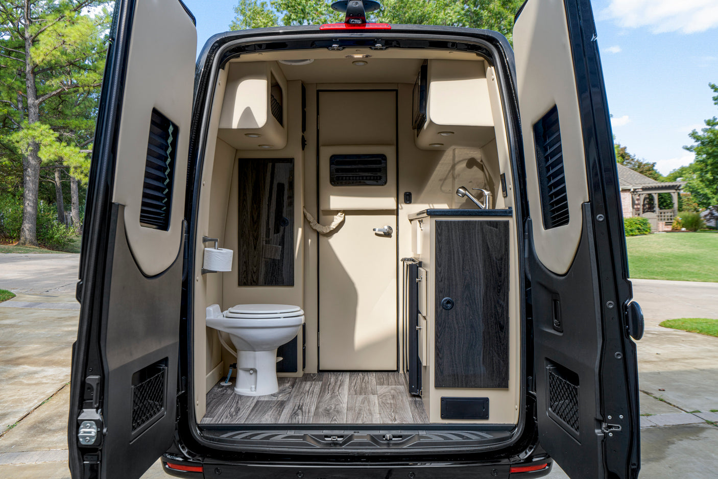 Interior of an RV rental: open rear doors reveal a camper van's compact kitchen, toilet, and storage inside.
