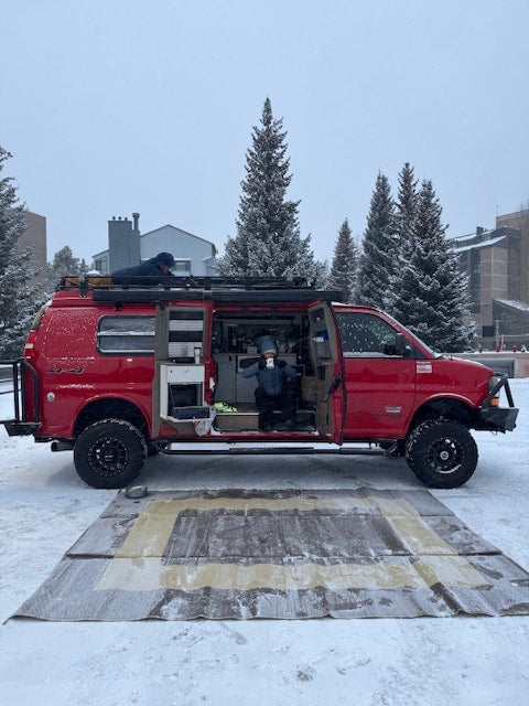 perfect for an outdoor escape or rv rental.|Red customized 4x4 rv rental van in snow. One person sips coffee inside