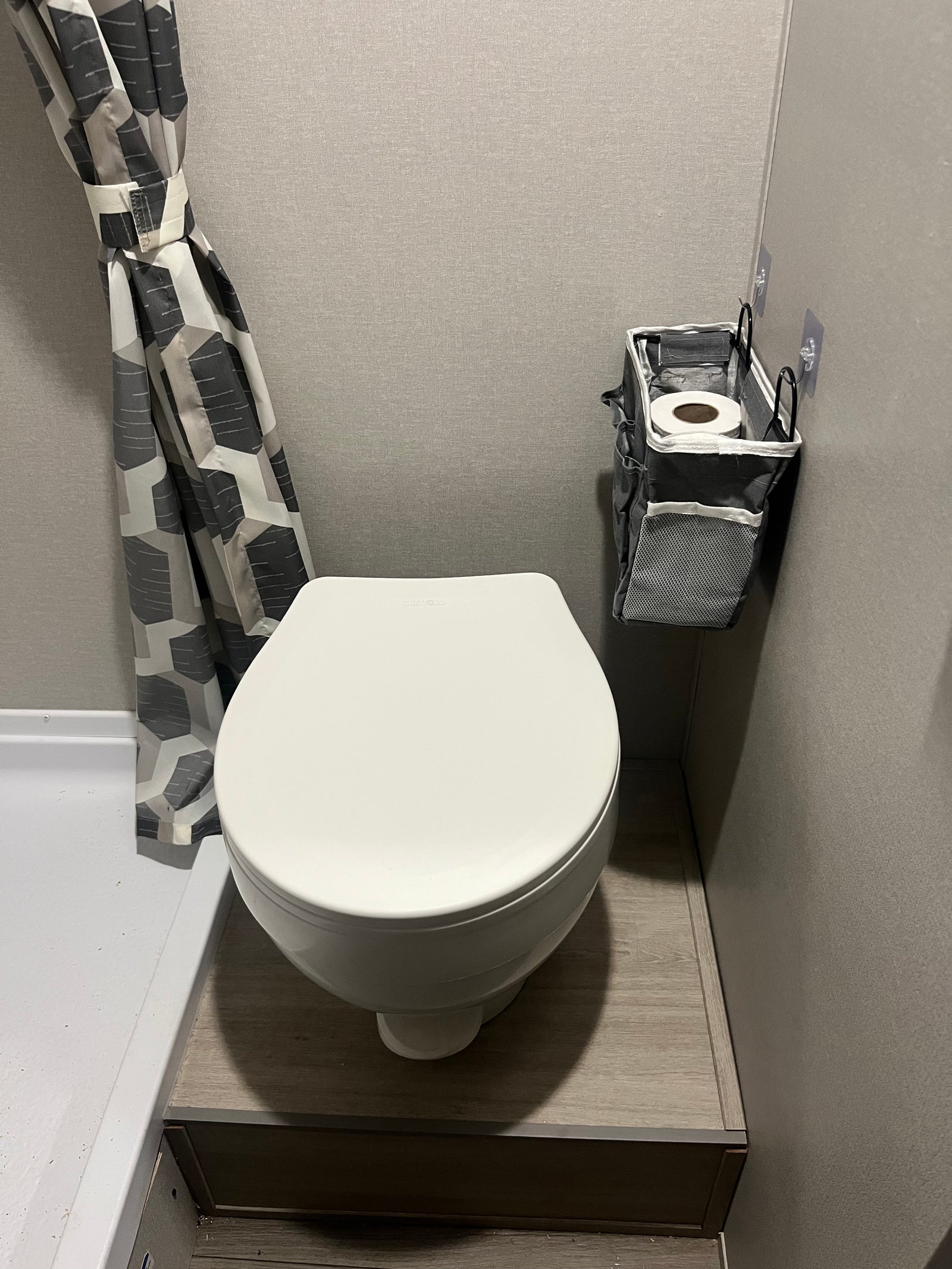 Compact RV rental bathroom featuring a white toilet, geometric shower curtain, and handy wall-mounted storage for essentials.