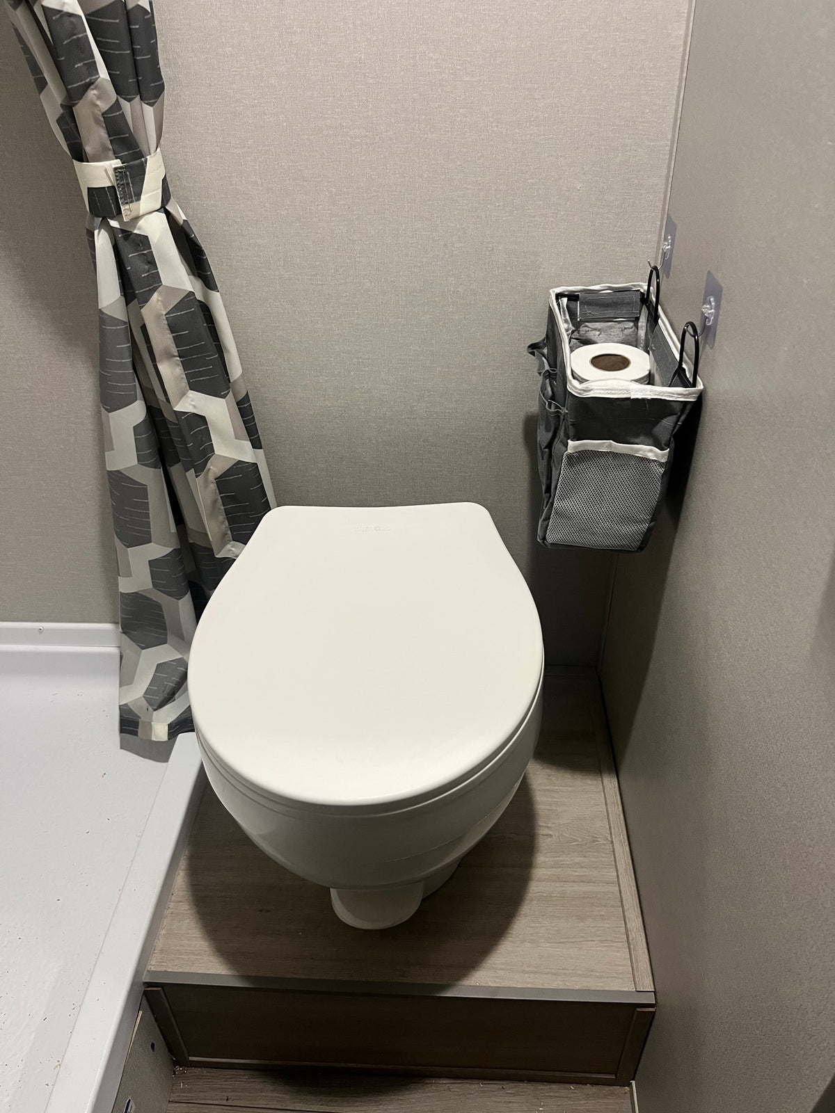 Compact RV rental bathroom featuring a white toilet, geometric shower curtain, and handy wall-mounted storage for essentials. — photo 8