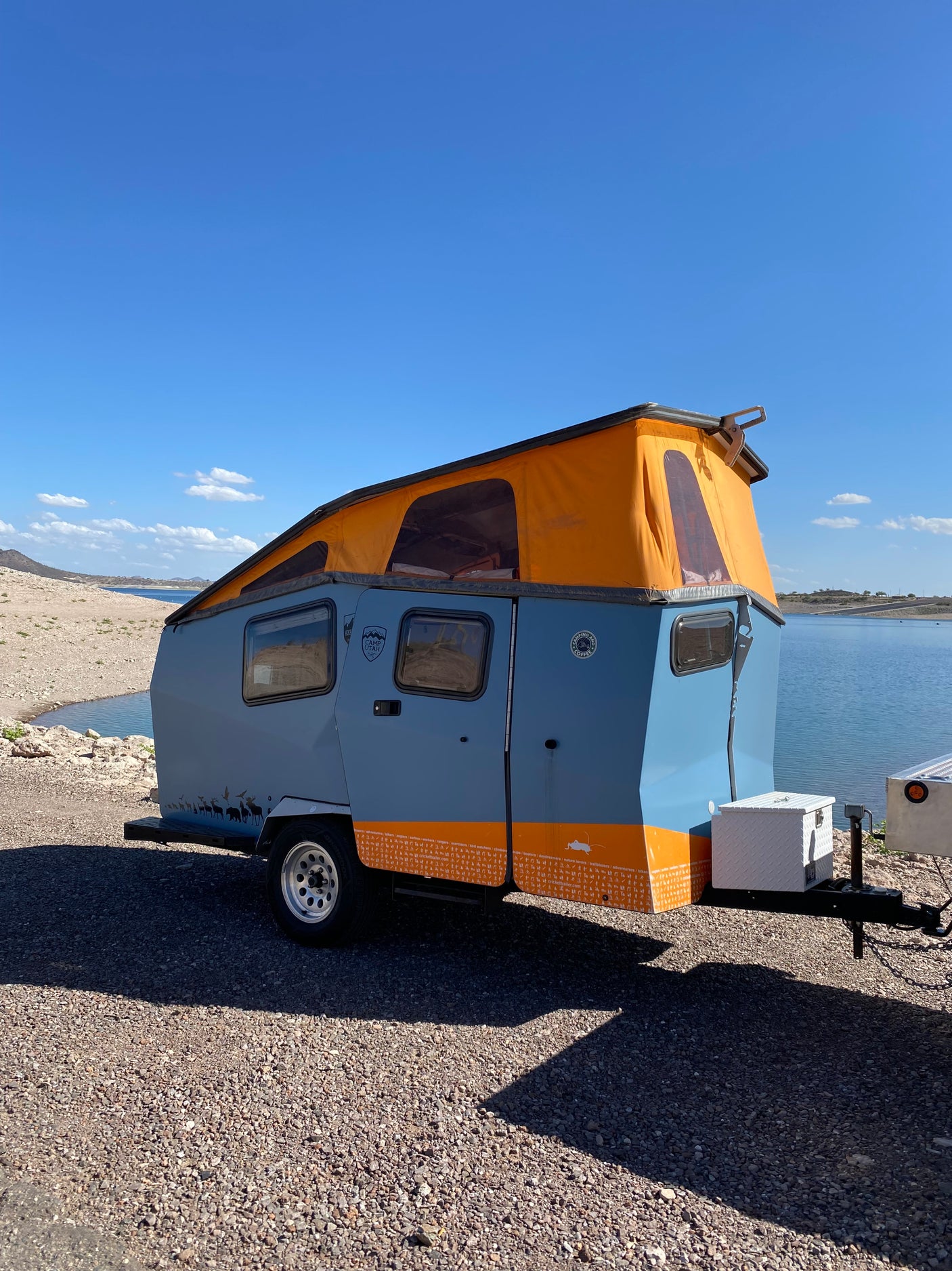 Lakeside RV rental: a stylish blue Cricket camper with an orange pop-top tent, perfect for outdoor adventures.