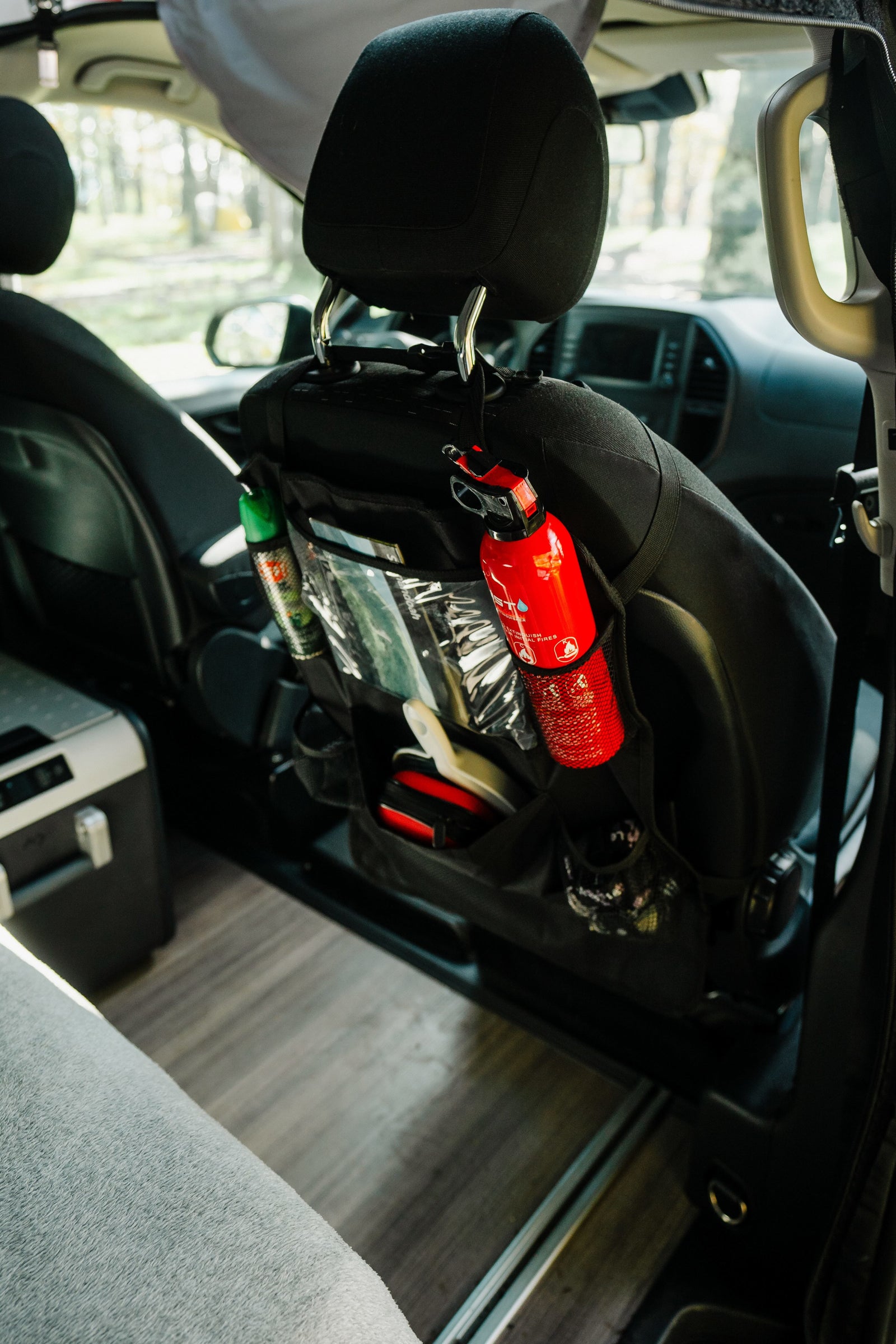 parked in autumn woods.|Cozy RV rental interior with a comfy bed and a beautiful nature view out the back window. Perfect for van life adventures!|Cozy RV rental pop-top bed. Soft gray bedding with a patterned sheet invites comfort inside this camper van.|RV rental ready: a trunk full of camping essentials including a portable table