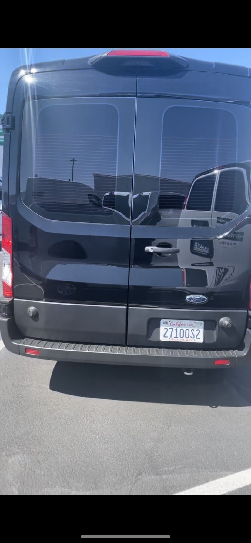 parked on asphalt. A building is visible in the background under a blue sky.|Black passenger van