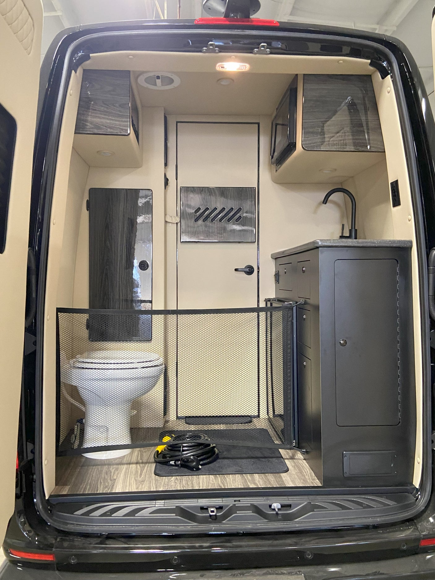 Explore this RV rental: a compact camper van interior with a toilet, kitchenette, storage, and a protective mesh gate.
