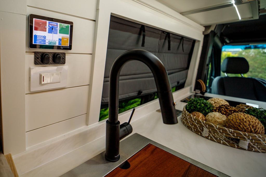 Sleek RV rental interior: black faucet, sink, smart power control panel, and decorative basket for modern comfort.