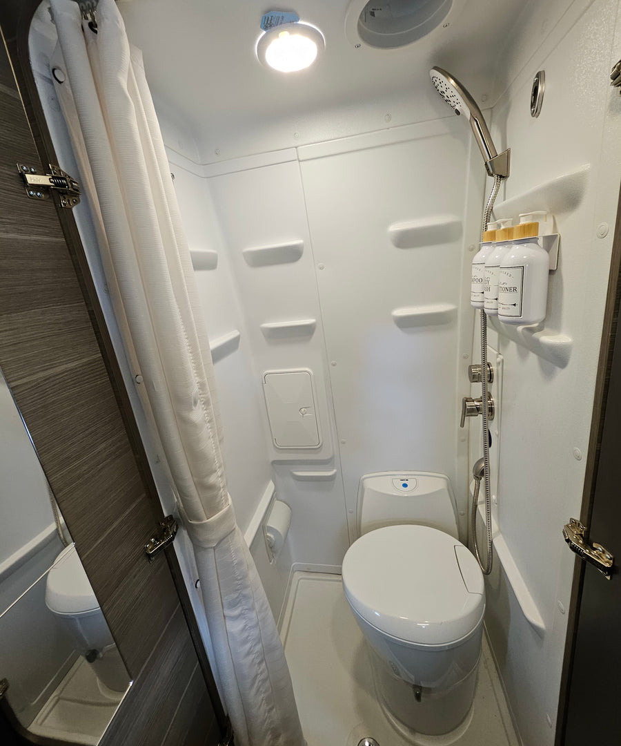 An RV rental's bright, compact bathroom showing a toilet, shower, and organized shampoo bottles.