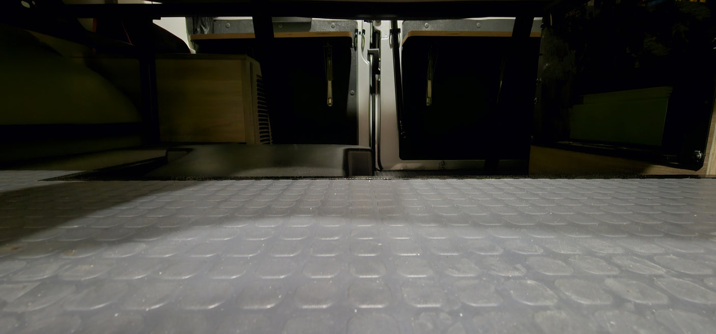 RV rental: Textured floor leads to organized storage under the bed in a camper van, showing hidden compartments.