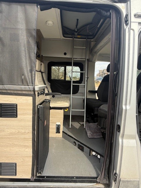 Inside this RV rental: a modern camper van interior with kitchen, ladder to overhead bed, and seating.