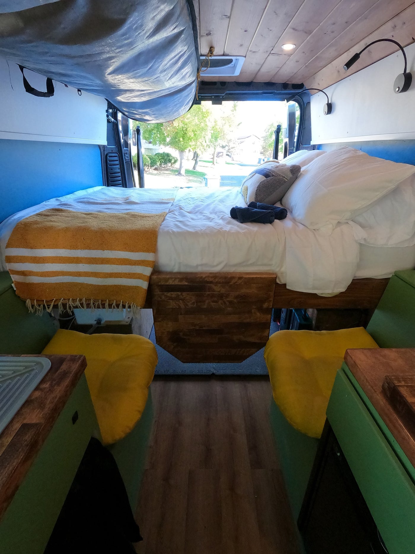 Inside an rv rental: a cozy bed with a yellow blanket, wooden accents, and open doors revealing nature views. — photo 16