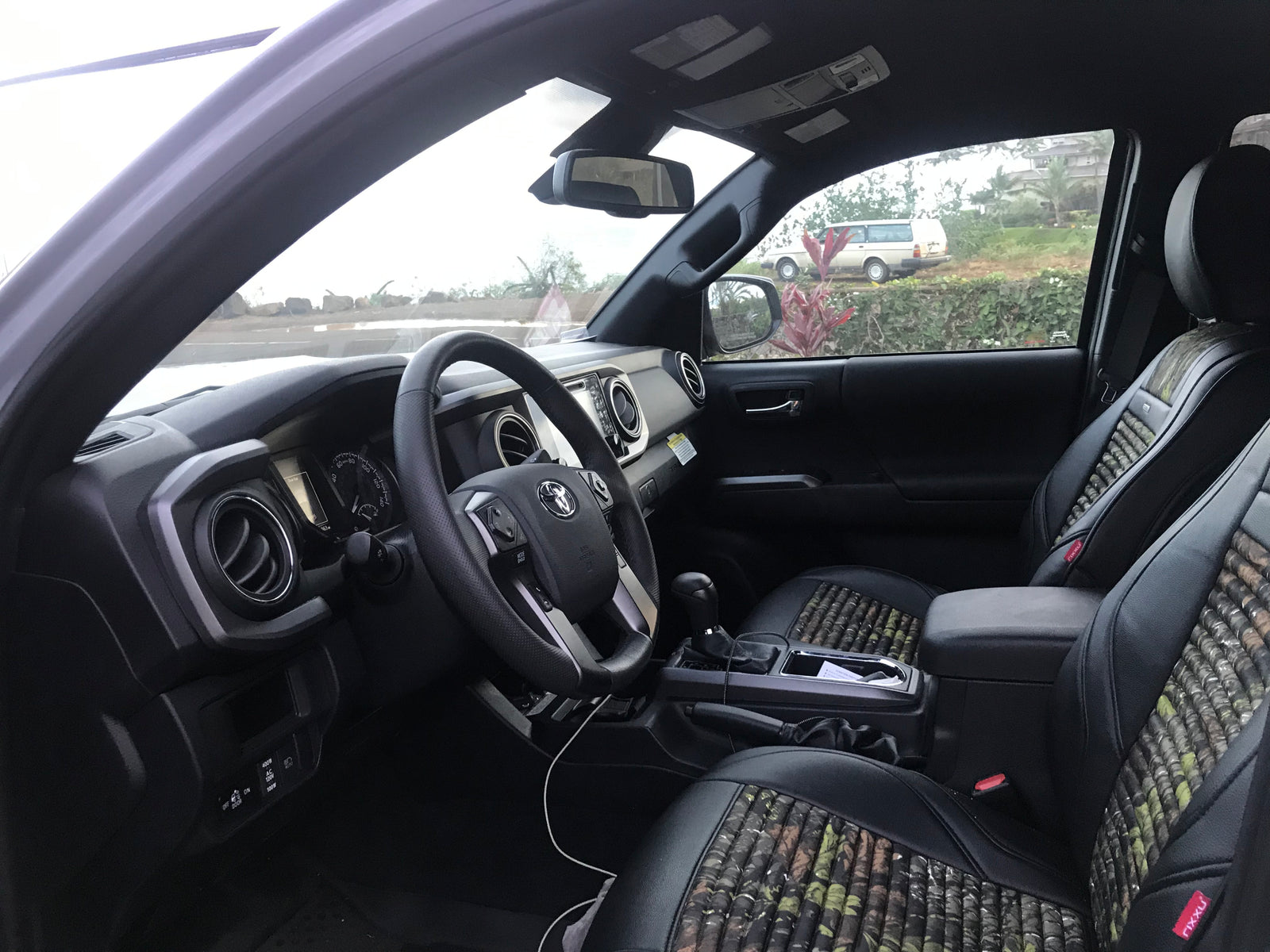 Toyota Tacoma interior. Patterned seats, dashboard, and view of a white vehicle resembling an RV rental outside.