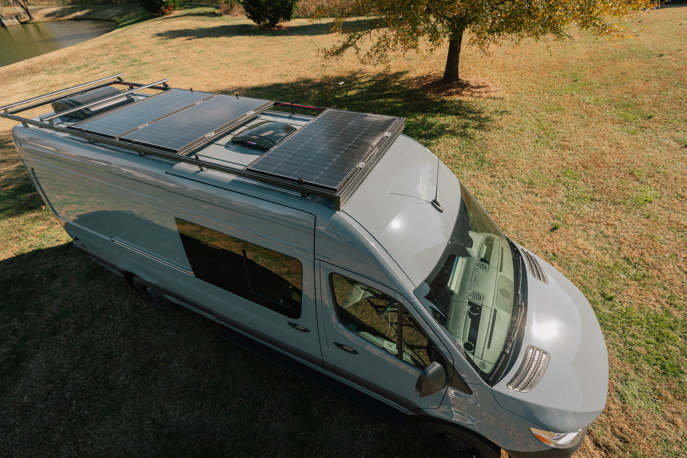 Overhead view: Light gray RV rental van with solar panels and rooftop AC unit, parked on grass.