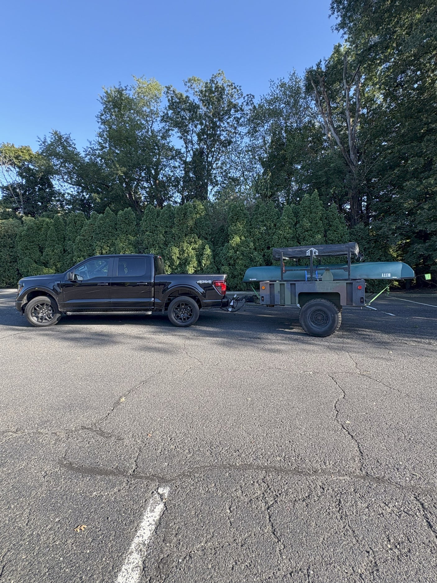 Black pickup truck towing a utility trailer with a canoe and rooftop tent, ready for an RV rental outdoor adventure.