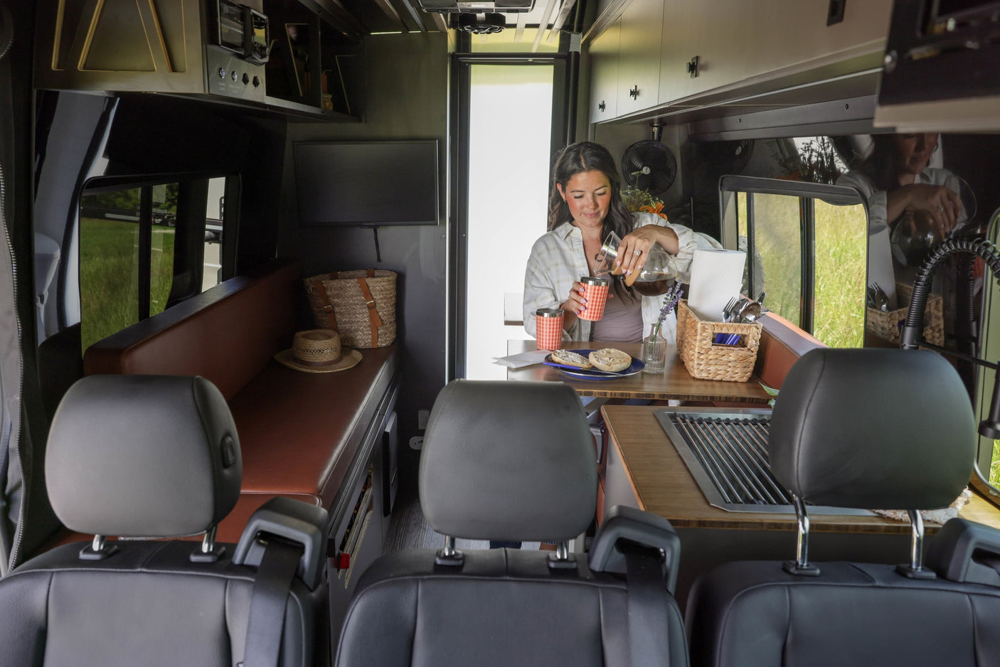 Woman pours coffee in a modern rv rental camper van, showcasing a functional kitchen and living area.
