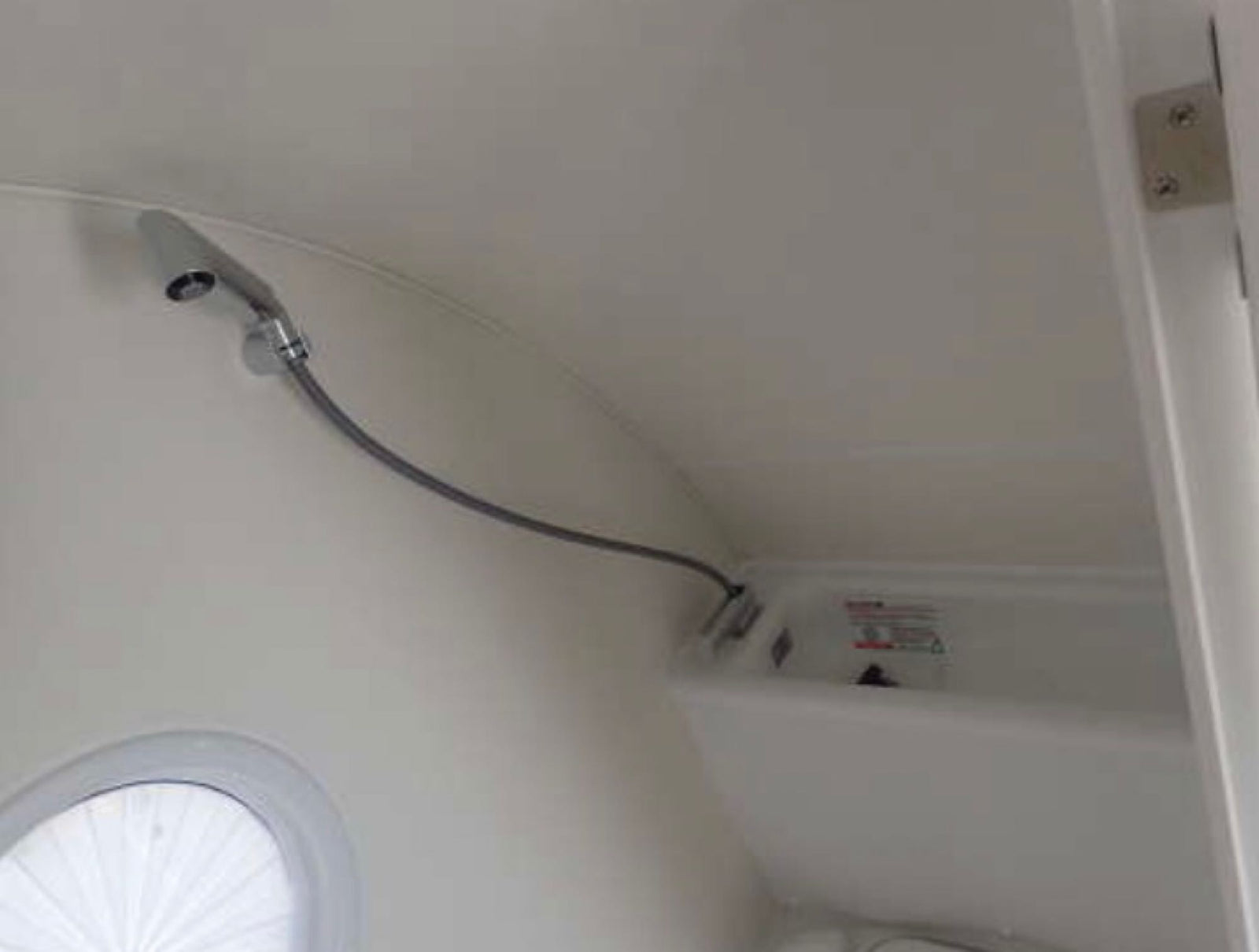 Compact shower and basin in an RV rental bathroom, featuring a flexible shower head and a round window.