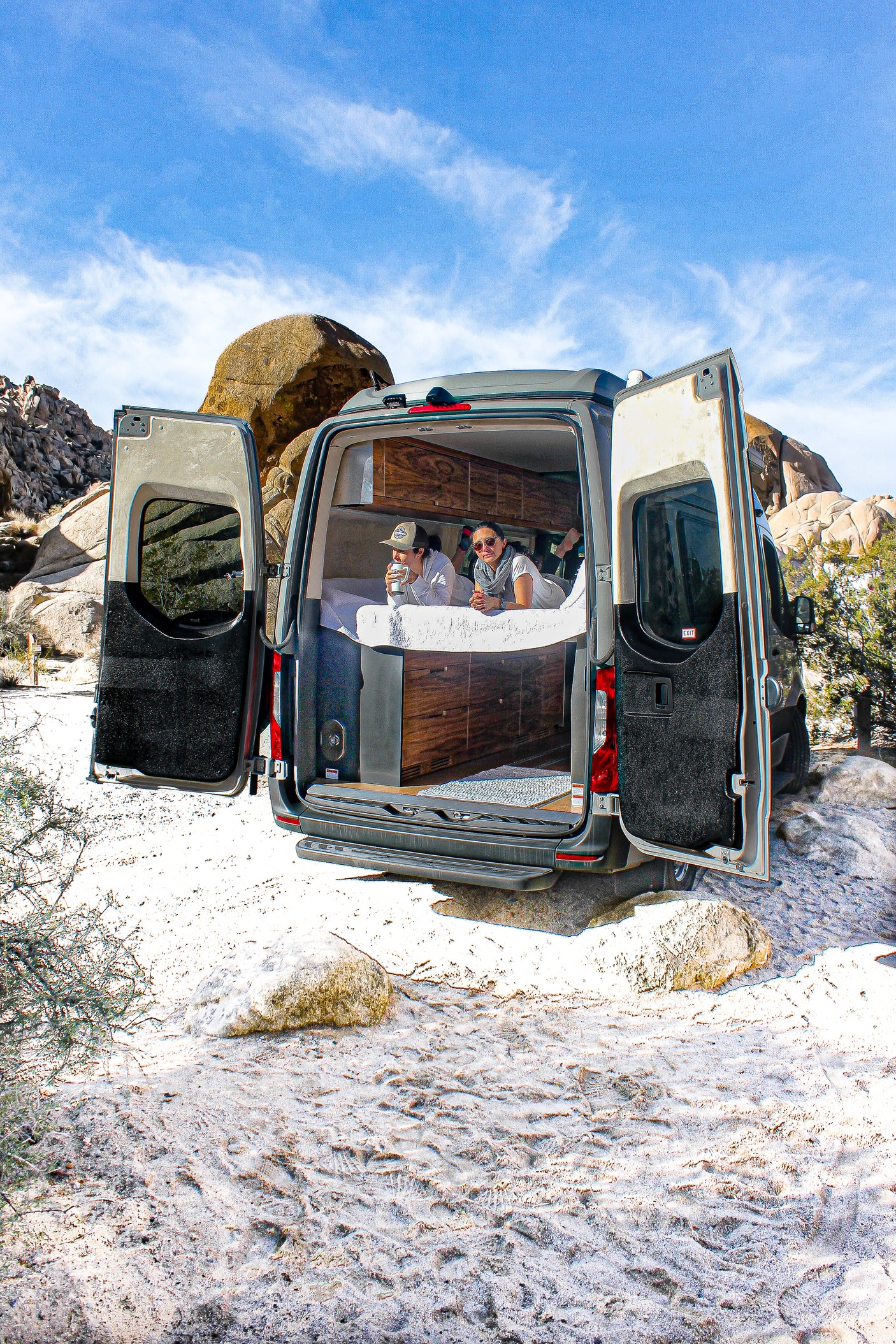 Relax in comfort on your next RV rental adventure! Two people enjoy the desert view from their camper van bed.