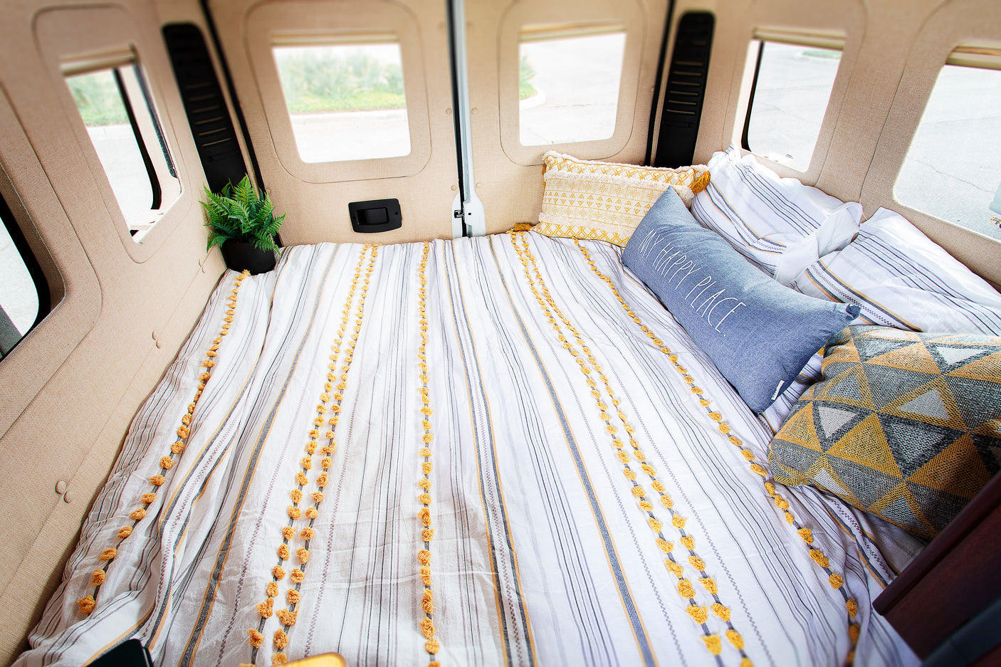 Cozy RV rental interior: A comfortable camper van bed with striped bedding, decorative pillows, and a plant.