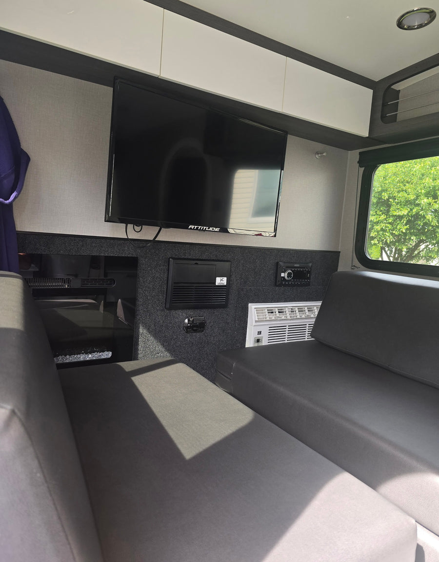 Inside an RV rental: a modern living space with a wall-mounted TV, cozy seating, and climate control features.
