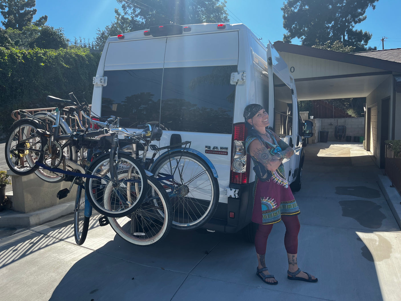 Smiling woman by a white Ram ProMaster camper van with bikes on the rear rack, perfect for an RV rental adventure.