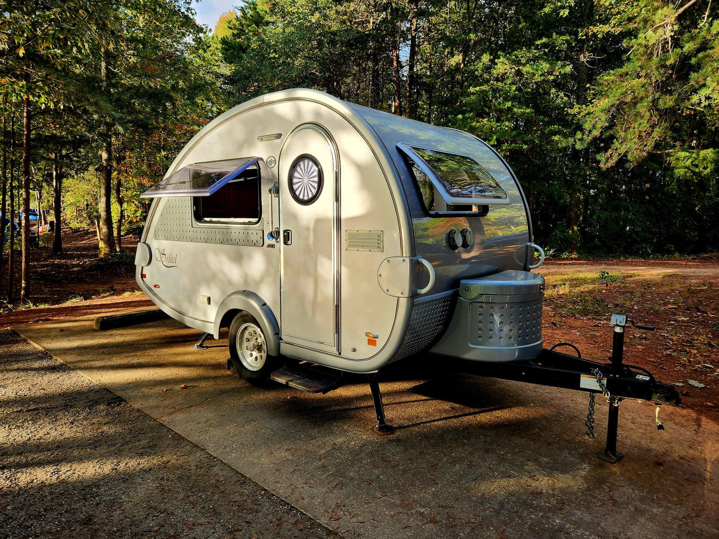 and front storage. Perfect for outdoor adventures.|This image features a stylish gray RV rental teardrop trailer parked at a scenic campsite under a vibrant sunset sky.|A sleek