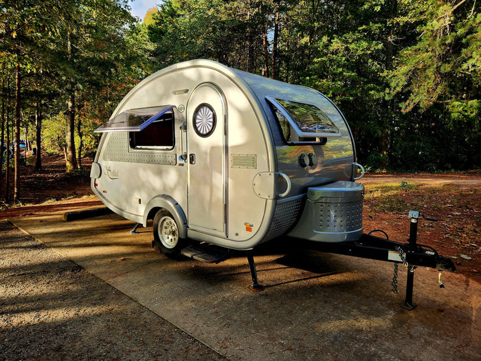 and front storage. Perfect for outdoor adventures.|This image features a stylish gray RV rental teardrop trailer parked at a scenic campsite under a vibrant sunset sky.|A sleek