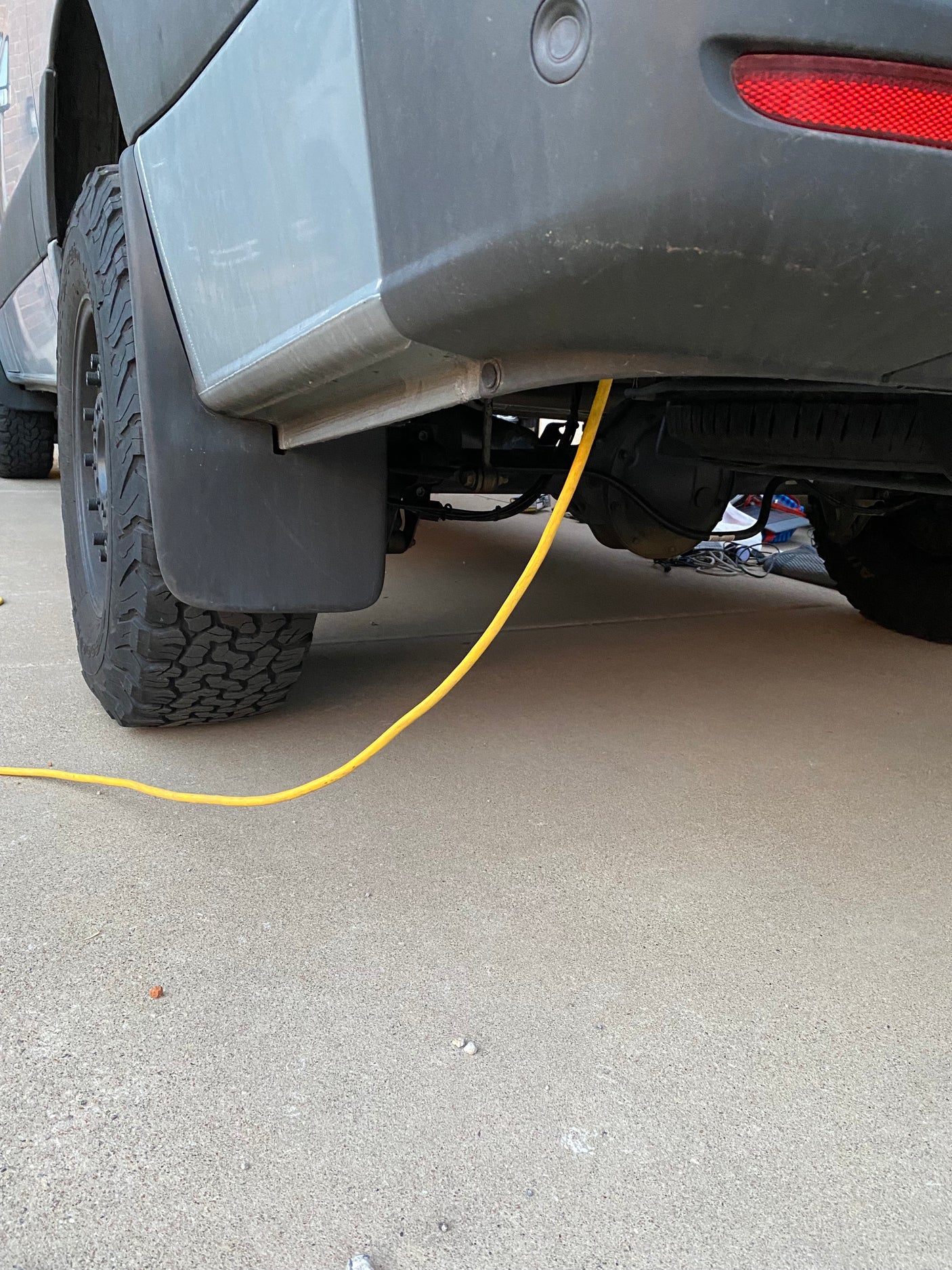 RV rental: A yellow power cable runs from the van's rear undercarriage to the concrete ground by the tire.