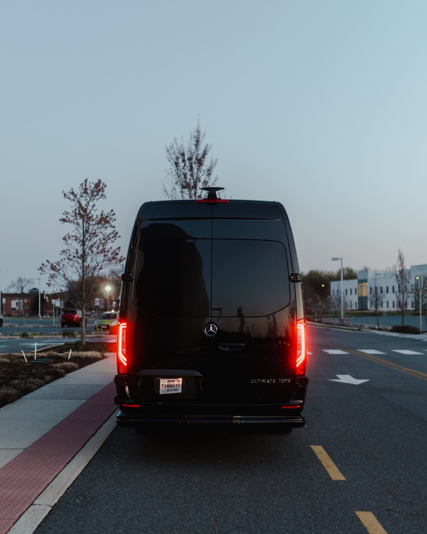 Black Mercedes-Benz Sprinter van, ideal for rv rental, seen from the rear at dusk with glowing red taillights and an Ohio plate.