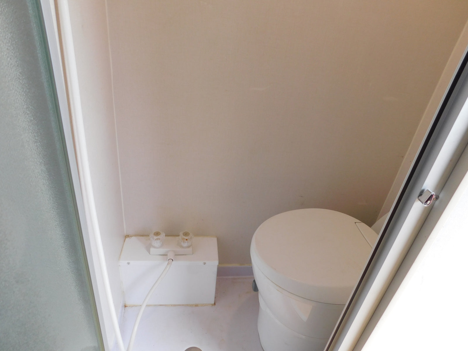 RV rental bathroom with compact shower area (controls & hose) and a round, self-contained toilet.