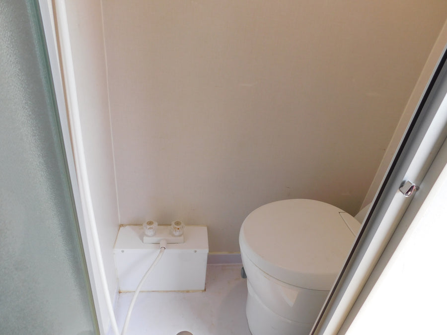 RV rental bathroom with compact shower area (controls & hose) and a round, self-contained toilet.
