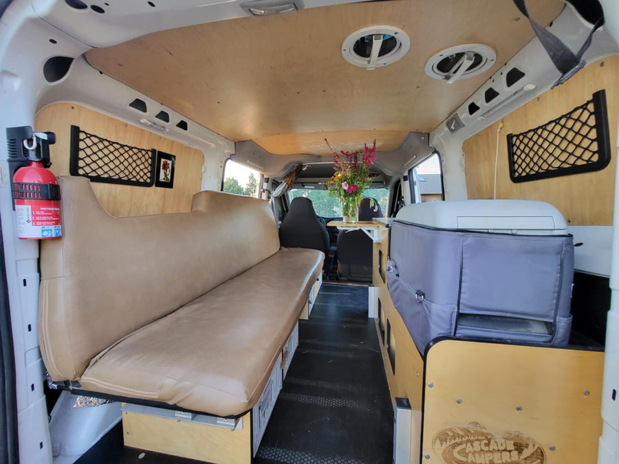 parked in a grassy field at sunset.|Inside a Cascade Campers RV rental: cozy seating